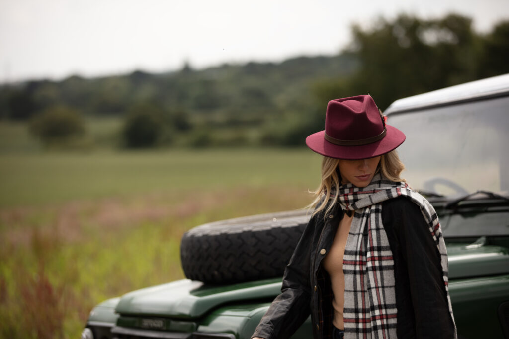 Woman wearing a red felt fedora in front of a Land Rover.